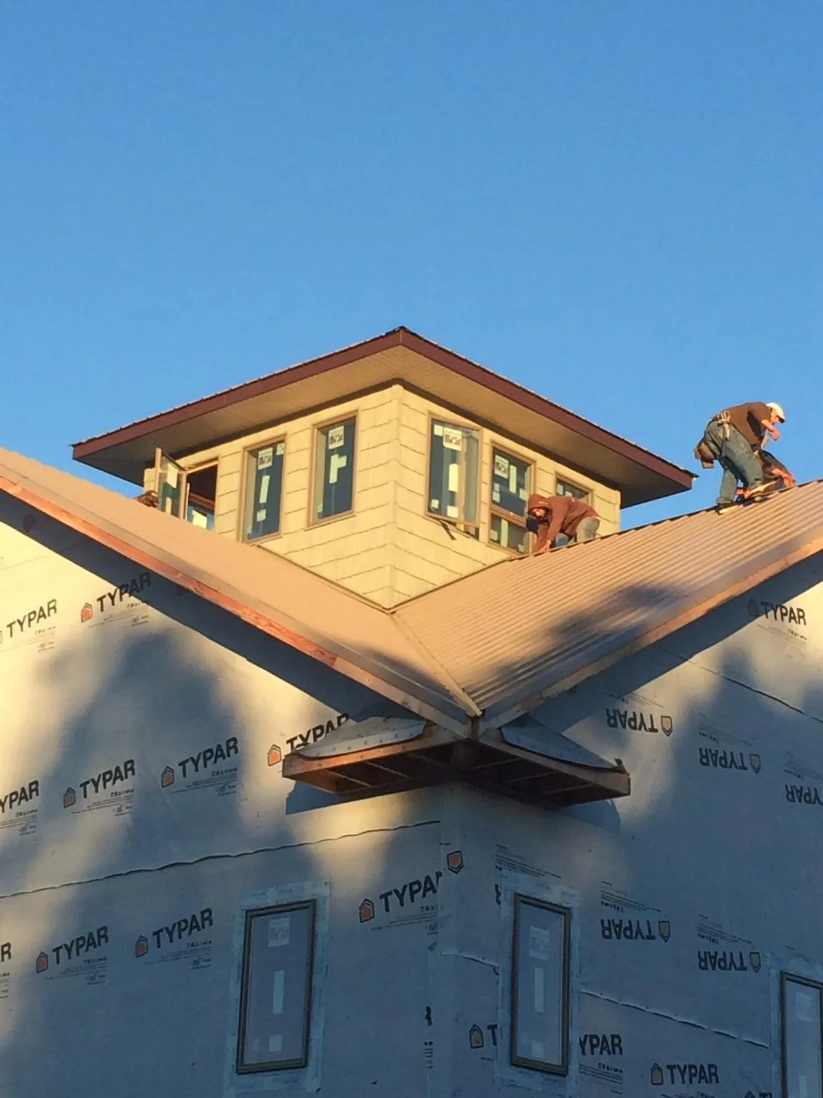 Roofers working around a rooftop cupola on a new metal roof at sunset — Roof Waterproofing in Woodbury by Roofing Brothers
